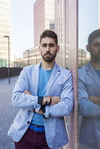 Portrait of handsome man with arms crossed standing by wall in city