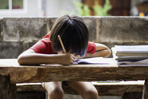 A girl sitting on a wooder table doing homework