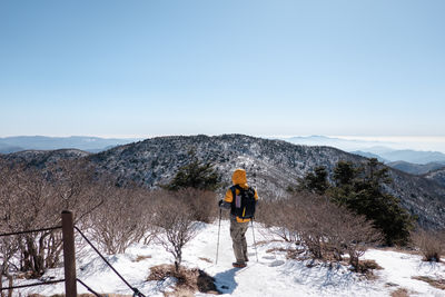 Rear view of man walking on mountain against clear sky