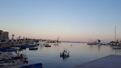 Sailboats moored in harbor at sunset