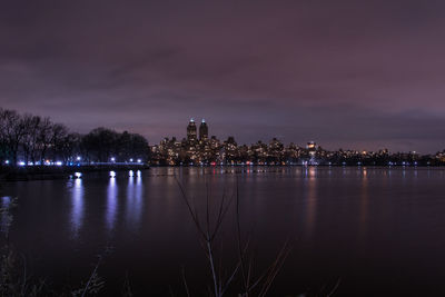 Illuminated city by river against sky at night