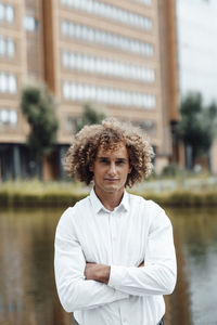 Confident businessman with arms crossed at riverbank