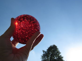 Low angle view of hand holding glass against clear blue sky