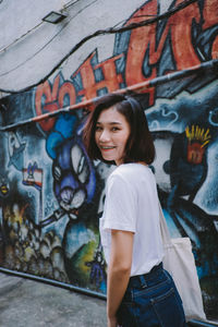 Portrait of teenage girl standing against graffiti wall