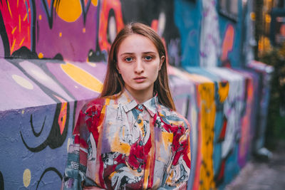 Portrait of young woman standing against graffiti