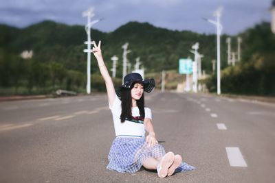 Full length of woman gesturing peace sign while sitting on road