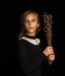 Portrait of a kid holding pussy willow brunches  against black background 