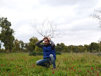 Man holding branch while crouching on poppy field