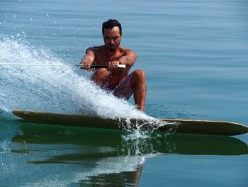 Full length of shirtless man wakeboarding in sea against clear sky