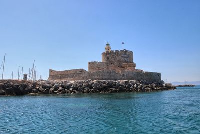 Lighthouse on building by sea against clear blue sky