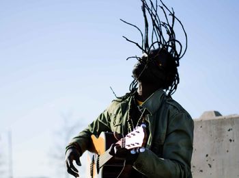 Man with tousled hair playing guitar against sky