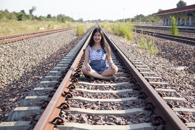 Full length of smiling woman sitting on railroad track
