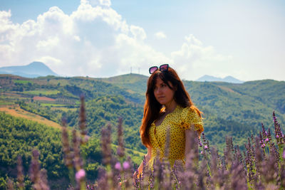 Young woman standing by flowers on mountain against sky