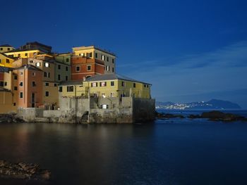 Buildings by sea against blue sky