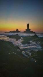 Silhouette of lighthouse at seaside during sunset