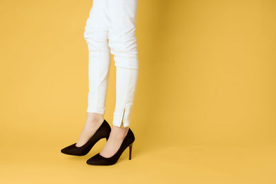 Low section of person wearing shoes standing against yellow background