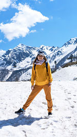 Happy young woman in  yellow  clothes standing on snow on background of mountain peaks, hiking 