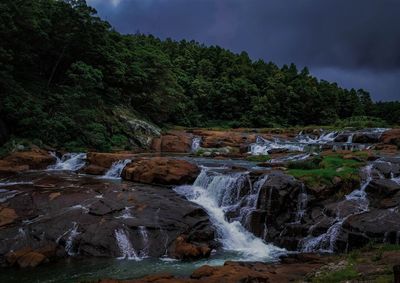 Scenic view of waterfall in forest against sky