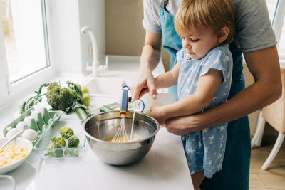 Mom teaches her little daughter how to make an omelet with vegetables.