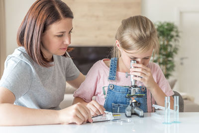 Girl looking through microscope sitting by mother at home