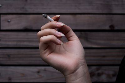 Close-up of hand holding cigarette against wall