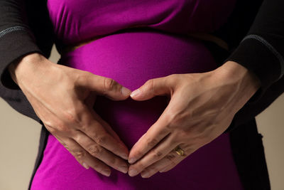 Midsection of pregnant woman with man making heart shape on stomach