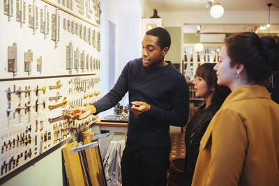 Young male sales clerk showing metal latches to female customers standing at home improvement store