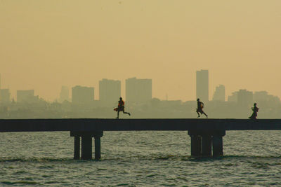 Silhouette people on bridge over sea against clear sky