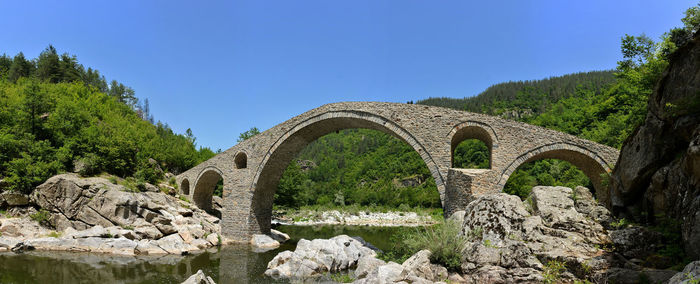 Arch bridge over rocks against clear blue sky