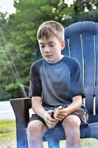 Boy sitting on armchair at back yard