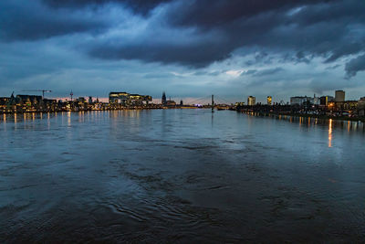 River by illuminated buildings against sky at dusk