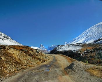 Road amidst snowcapped mountains against clear blue sky