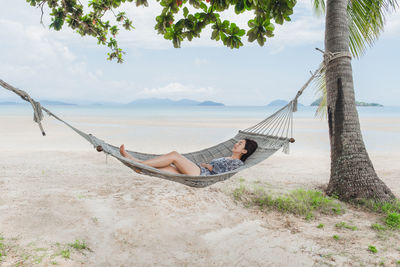 Man relaxing on hammock at beach against sky