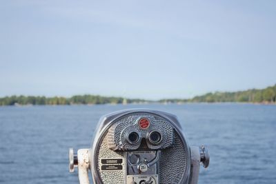 Close-up of coin-operated binoculars by sea against sky