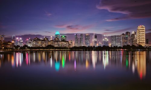 Illuminated buildings by lake against sky in city at night