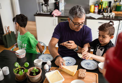 High angle view of father and son applying butter on crackers at dining table