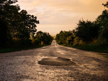 Road amidst trees against sky during sunset