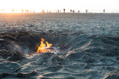 Close-up of fire at beach against sunset 