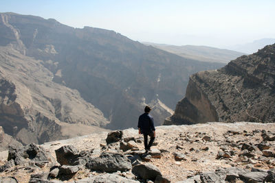 Rear view of man standing on rocks against mountains