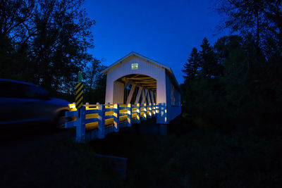 Blurred motion of car moving towards covered bridge against blue sky at night