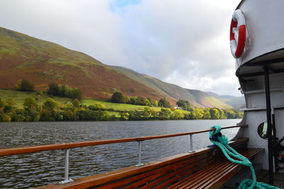 Cropped image of boat sailing in river by mountain against sky