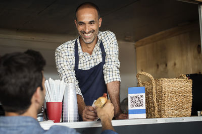 Smiling male vendor giving hotdog to customer at food truck