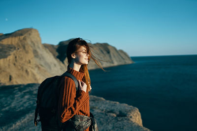 Man standing on rock by sea against sky