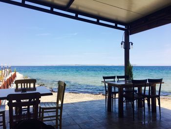 Empty chairs and table by sea against sky