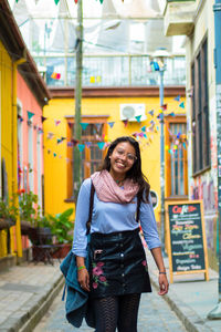 Portrait of smiling young woman standing on narrow street