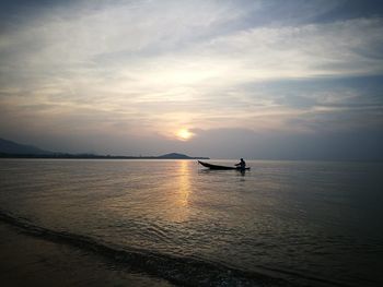 Silhouette man in sea against sky during sunset