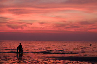 Silhouette man standing on beach against orange sky