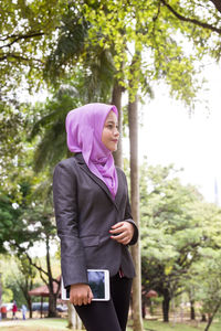 Young woman holding digital tablet while walking at park