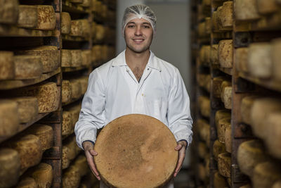 Cheese factory worker proudly holding loaf of cheese