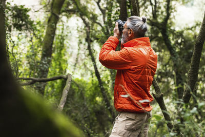 Senior male explorer photographing with camera in forest during weekend